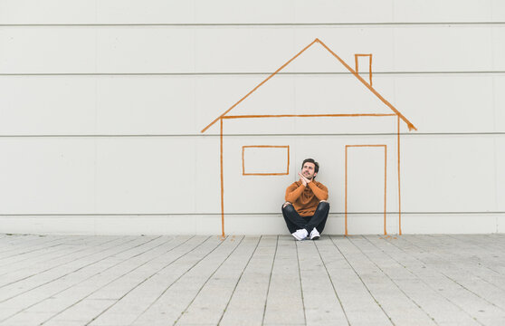 Digital composite of young man sitting at a wall with a house