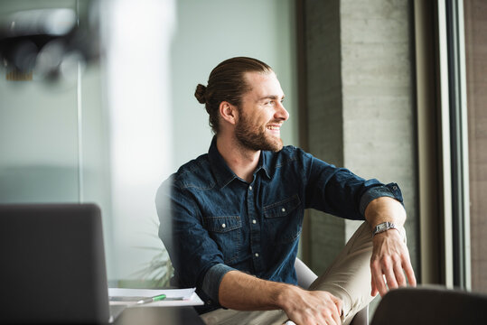 Smiling businessman sitting in office looking out of window