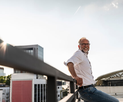 Mature man standing on roof of a high-rise building, leaning on railing