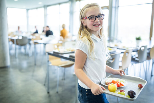 Portrait of smiling schoolgirl carrying tray in school canteen
