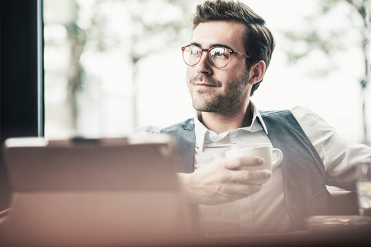Smiling young man in a cafe with tablet and cup of coffee