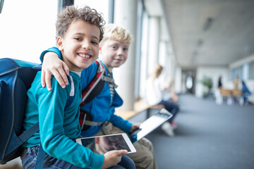 Portrait of two smiling schoolgboys with tablet embracing