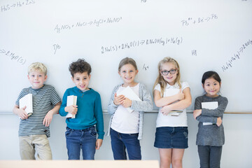 Portrait of smiling pupils standing at whiteboard with formulas in class