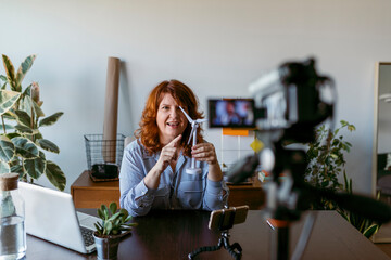 Woman making vlog with home video camera while sitting by table at home