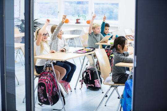 Happy pupils raising their hands in class