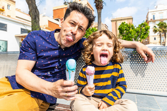 Spain, Barcelona, happy father and son sitting on bench enjoying an ice cream