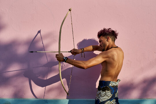 Barechested young man with bow and arrow outdoors