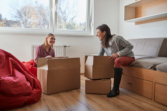 Two happy young women unpacking cardboard boxes in a room
