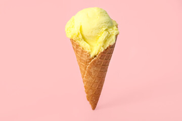 Delicious yellow ice cream in waffle cone on pink background