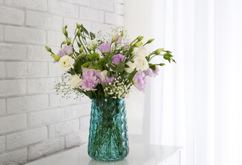 Bouquet of beautiful Eustoma flowers on table near white brick wall