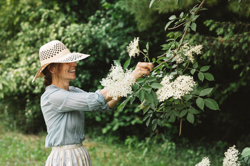Smiling woman picking flower from flowering plant while standing in garden