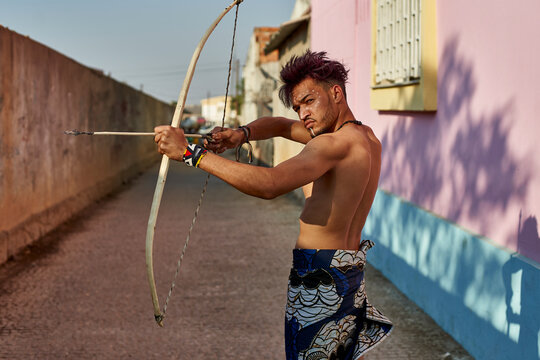 Barechested young man with bow and arrow outdoors