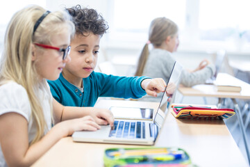 Schoolboy and schoolgirl using laptop together in class
