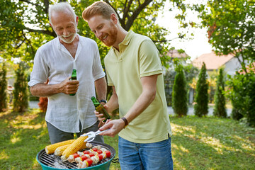 Senior father and adult son having a barbecue in garden