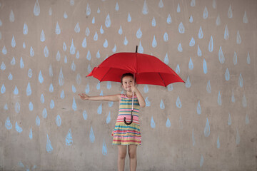 Girl holding a red umbrella standing next to a concrete wall with rain drop chalk drawings