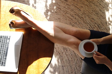 Woman with her legs up on desk with a herbal tea and laptop with sun streaming in window