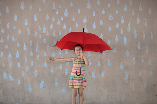 Girl holding a red umbrella standing next to a concrete wall with rain drop chalk drawings