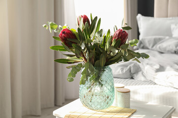 Vase with bouquet of beautiful Protea flowers on white table in bedroom