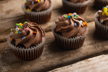 Close-up view of tasty chocolate cupcakes with sprinkling on rustic wooden background with yellow lights. Sweet dessert. Bakery concept. Elegant food. Sweets for coffee or tea. Flat lay.
