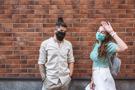 Couple wearing protective face masks while standing against brick wall during COVID-19