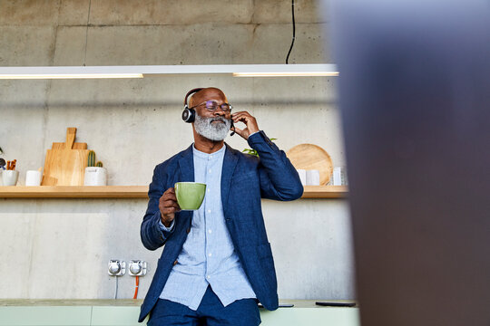Man with eyes closed listening to music while drinking coffee at home