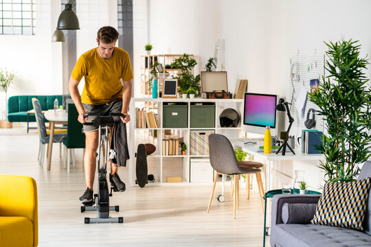 Young man looking down while cycling on exercise equipment at home