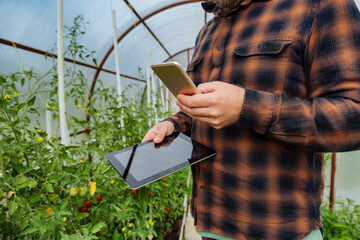 Man holding digital tablet while using mobile phone at greenhouse