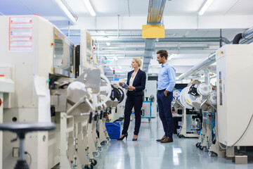 Male technician standing near businesswoman analyzing machinery at factory
