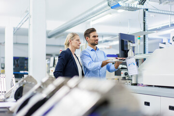 Businessman using computer on machinery while discussing with businesswoman in illuminated factory