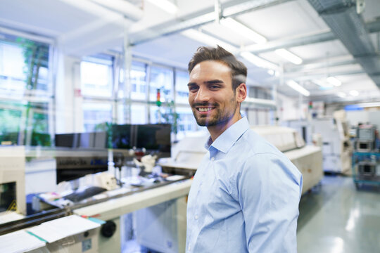 Smiling young male technician standing at illuminated factory - Powered by Adobe