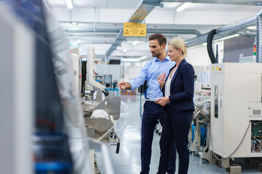 Confident young engineer discussing with businesswoman while pointing at machinery in factory