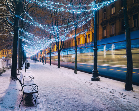 Blurred motion of tram by snow covered footpath in illuminated city during Christmas