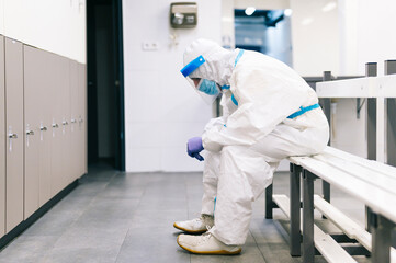 Thoughtful man wearing protective suit sitting on bench in hospital