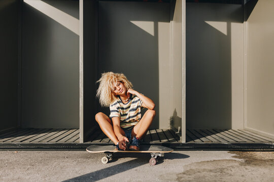 Woman with skateboard sitting against metallic cabins on sunny day