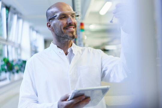 Smiling male scientist looking at sample while holding digital tablet in factory