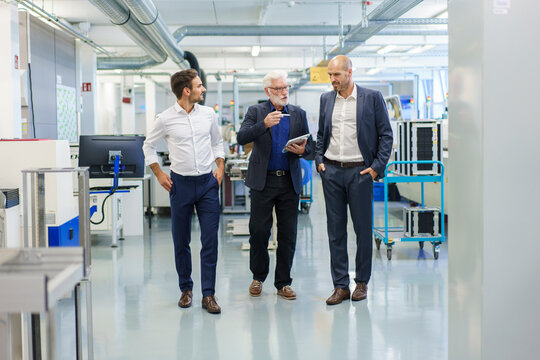Senior manager with colleagues discussing over digital tablet while walking at illuminated factory
