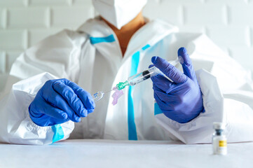 Nurse wearing protective suit filling injection while sitting by table in hospital