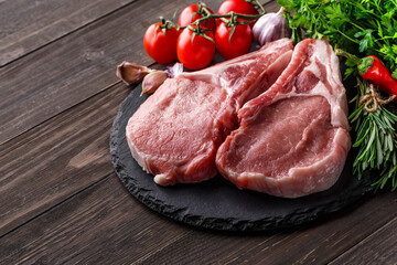 Raw fresh meat steak with cherry tomatoes, hot pepper, garlic, oil and herbs on dark stone, concrete background.Top view.Rustic style.