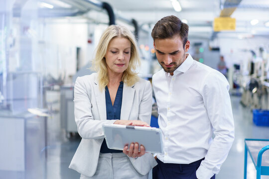 Confident blond businesswoman discussing over digital tablet with male colleague at factory - Powered by Adobe