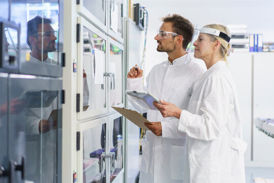 Young male technician analyzing while standing by female colleague at illuminated laboratory