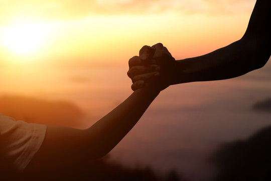 Silhouette of giving a helping hand, hope and support each other over sunset background.