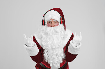 Santa Claus with headphones listening to Christmas music on light grey background