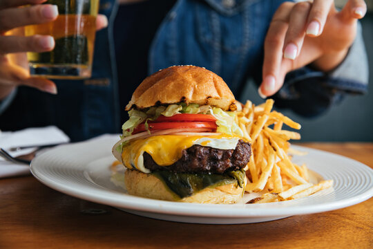Hand Grabbing Cheeseburger with two types of Cheese and French Fries and Drinking a Beer