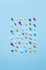 Creative layout of colorful pills and capsules on blue background with summer sun and sharp shadow. Minimal medical concept. Pharmaceutical, Covid-19 or Coronavirus. Flat lay, top view, copy space.
