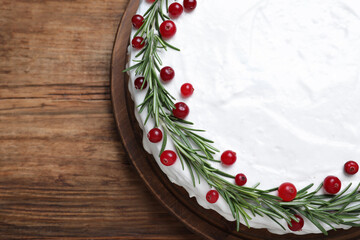 Traditional Christmas cake decorated with rosemary and cranberries on wooden table, top view