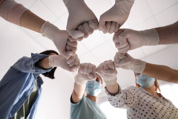 People in white medical gloves joining fists on light background, low angle view