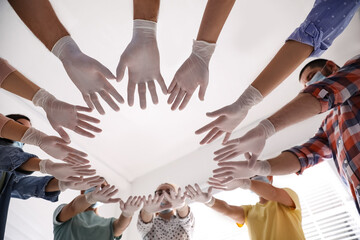 People in white medical gloves joining hands on light background, low angle view