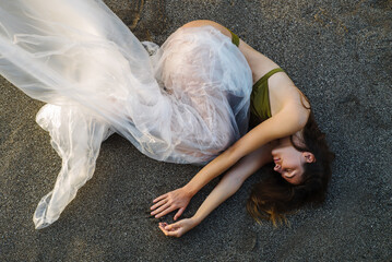 The girl is wrapped in plastic film and lies on the black sand on the beach
