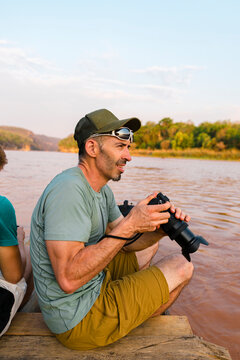 Side view of tourist holding digital camera on a piroque at sunset