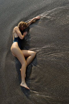 Girl in a swimsuit lies on the black sand